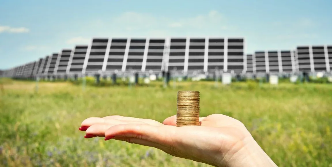 Een hand die munten vasthoudt voor een grasveld vol met Solar Power Systems zonnepanelen. Energiebeheer oplossingen