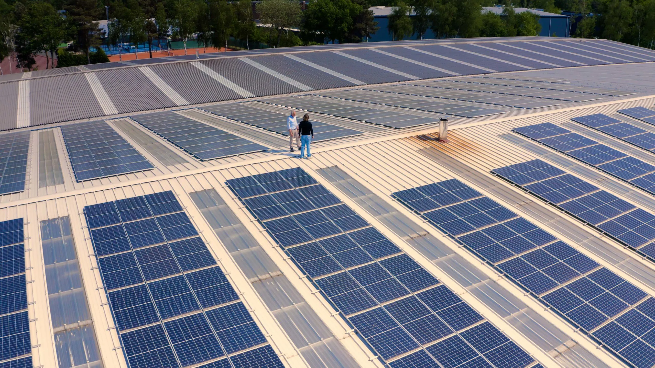 Luc Martens van Solar Power Systems die samen met de klant op een dak van een bedrijf vol zonnepanelen staat.